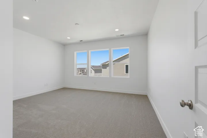 Spacious room featuring neutral carpeting, white painted walls, three large windows, and recessed lighting