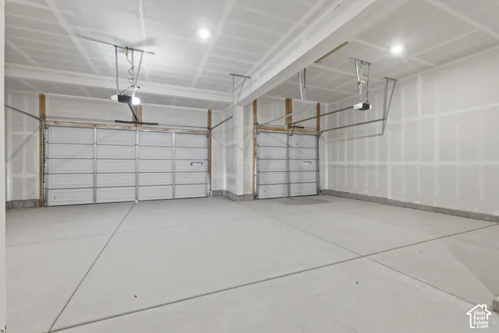 Two vehicle bays with automatic garage door openers and concrete flooring
