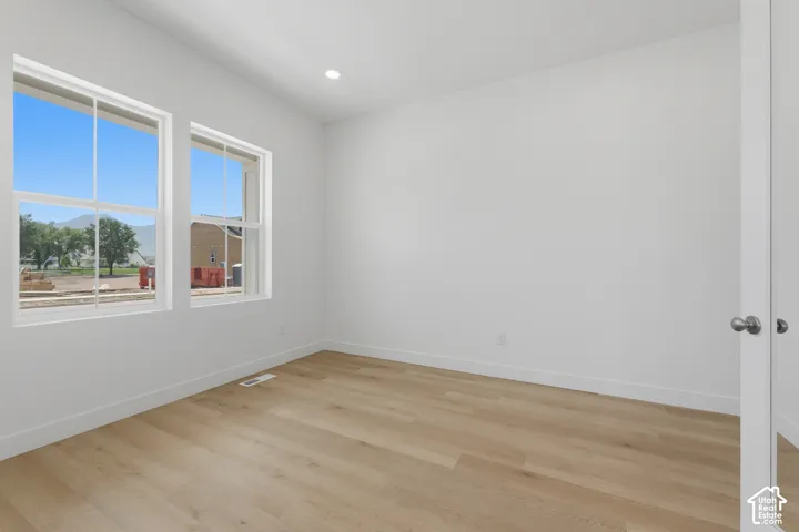 Recessed lighting illuminates the space, featuring two large windows, wood-finish flooring, and white trim