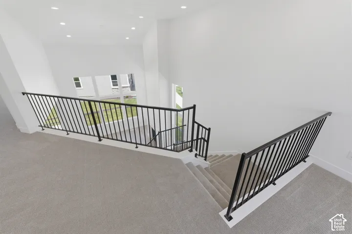 Carpeted staircase with black metal railings, recessed lighting, and white walls