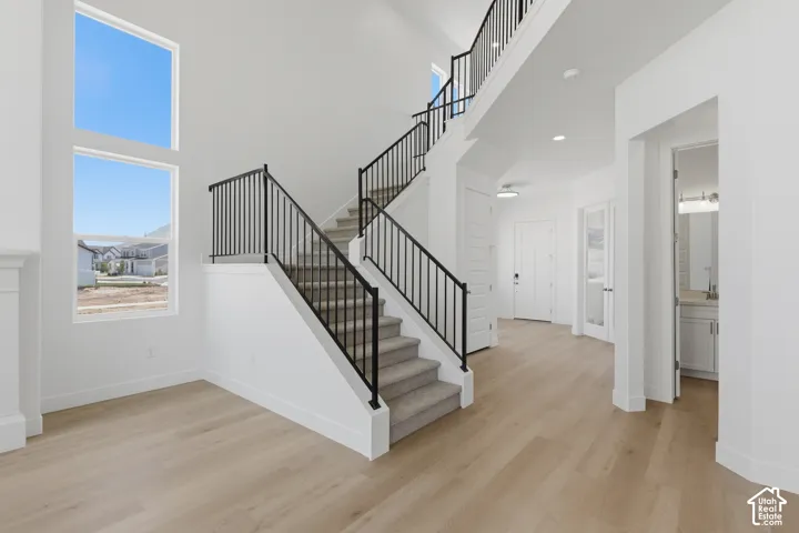 Two-story entry with high ceilings, wood-finish flooring, and a carpeted staircase with an iron railing
