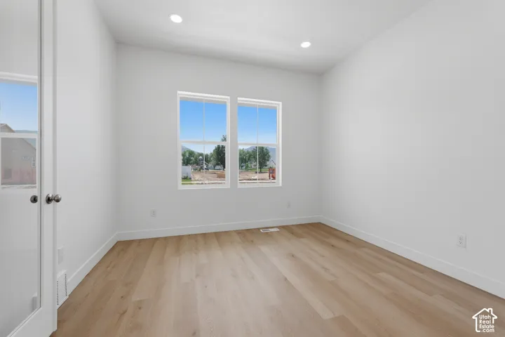 Recessed lighting, wood-finish flooring, two large windows, white walls, and a glass-paneled door