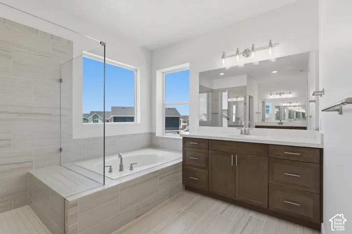 Spacious bathroom featuring a built-in soaking tub, separate glass-enclosed shower, dual vanity with white countertop, and light tile flooring