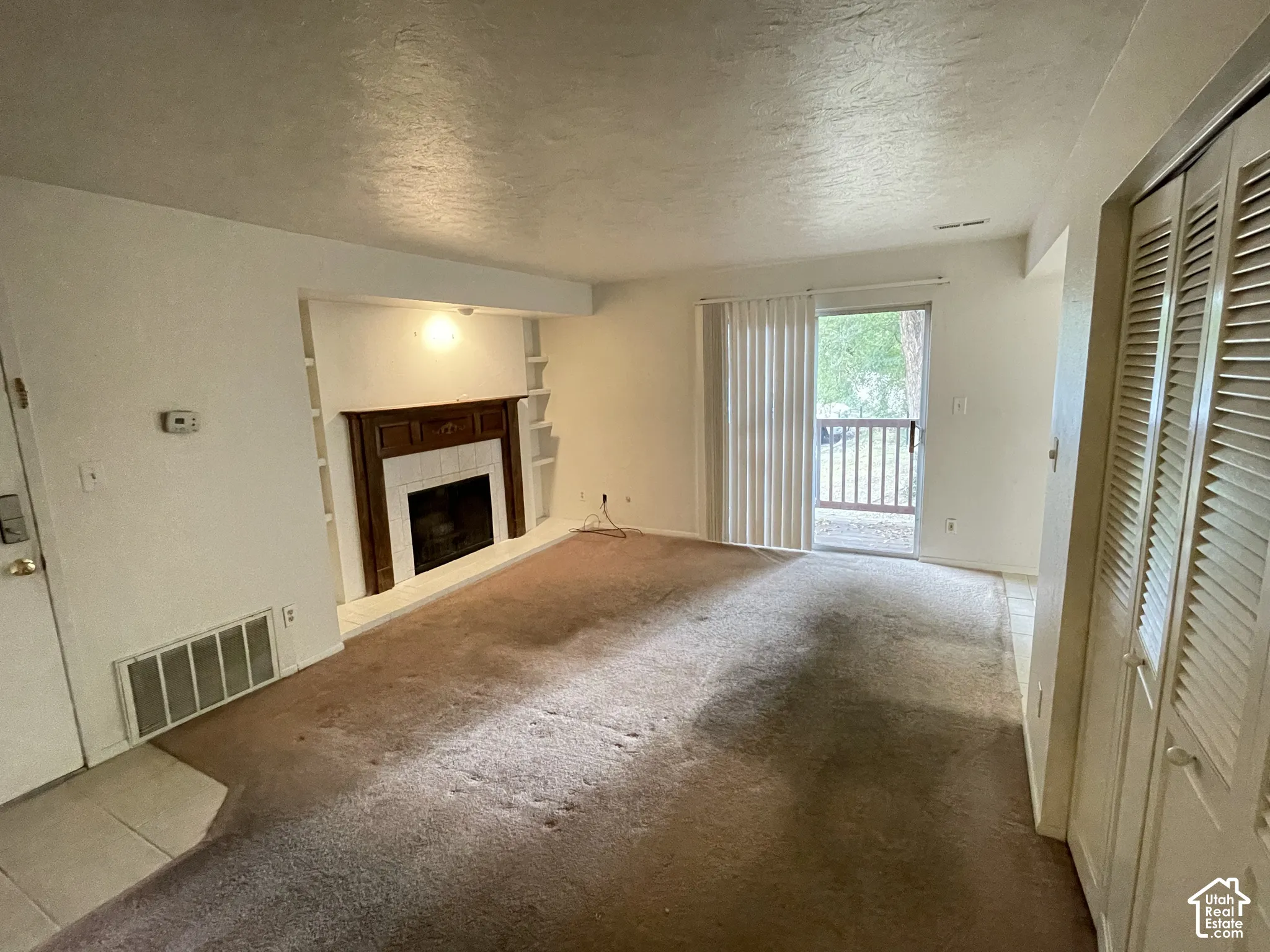 Living area featuring a fireplace with a wood-finish mantel and tile surround, built-in shelving, sliding glass door with vertical blinds, and louvered bifold doors