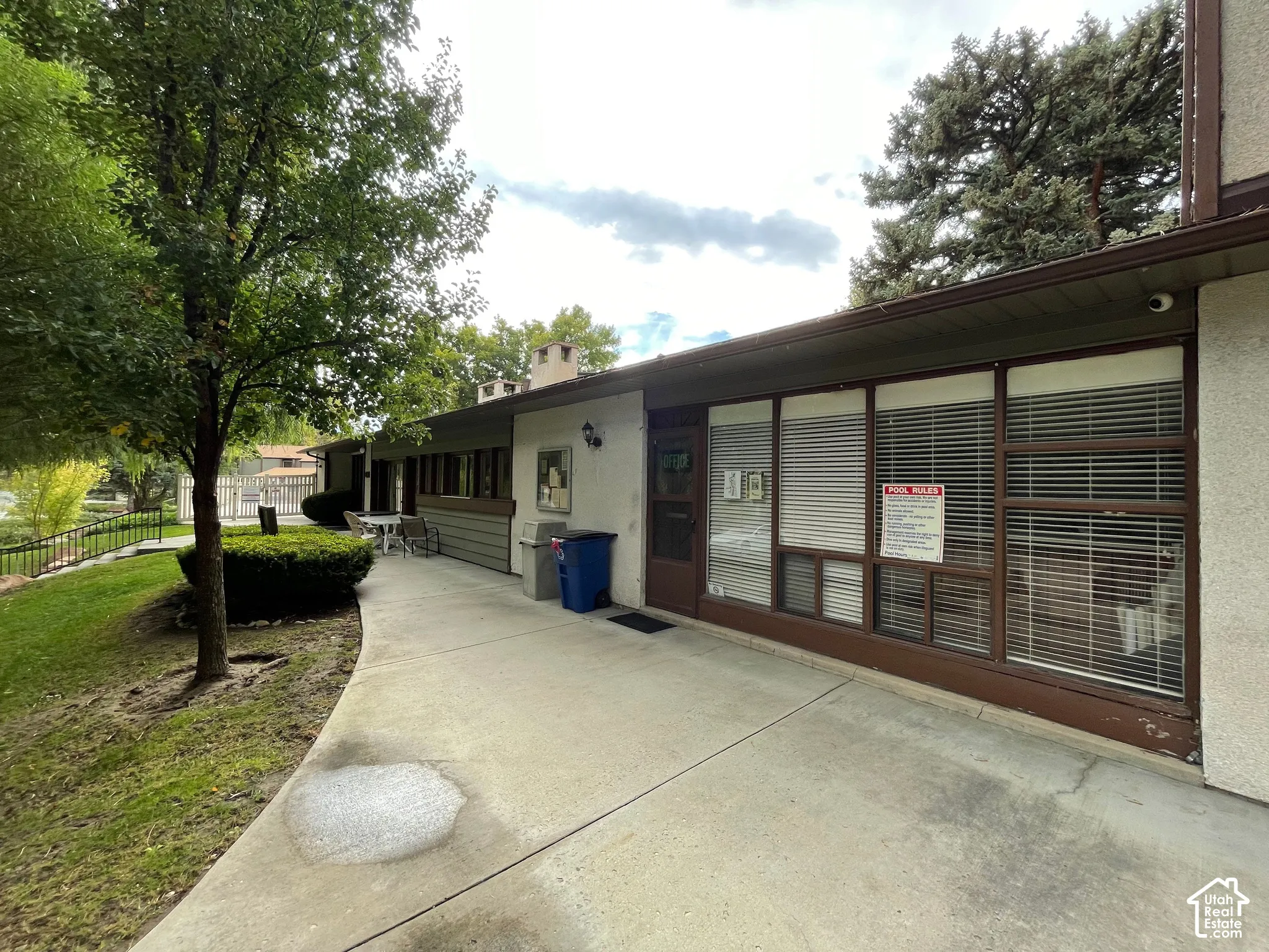 Exterior building with a concrete walkway, multiple windows with blinds, and a brown entry door