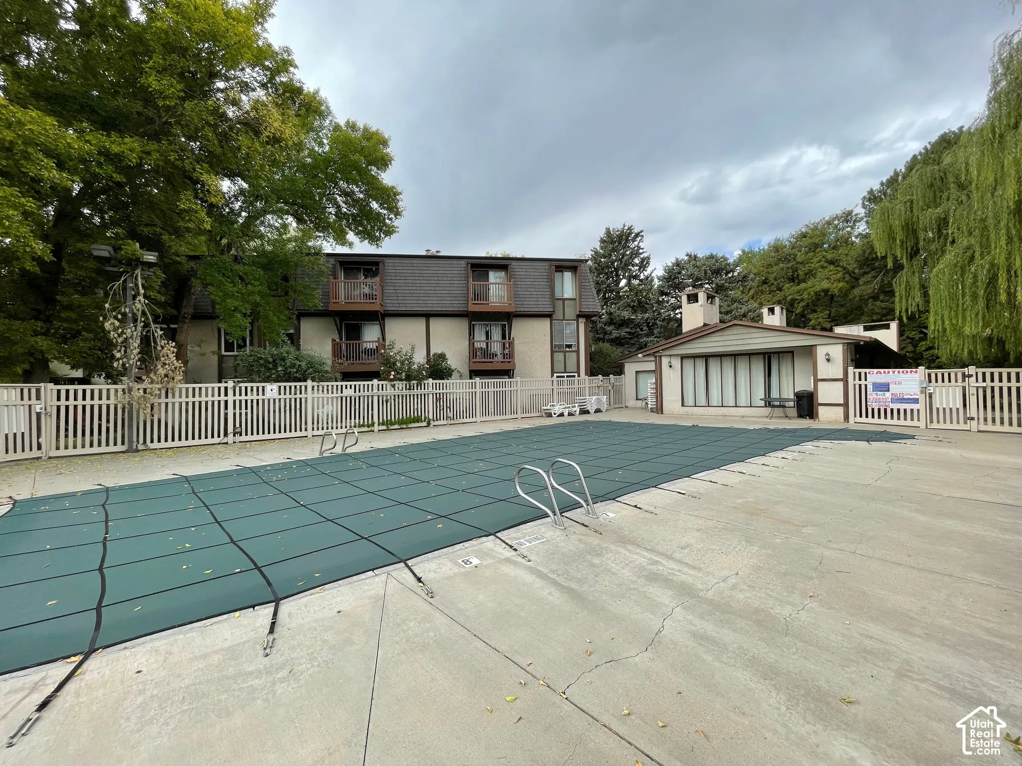 Community pool with a green pool cover and concrete surround
