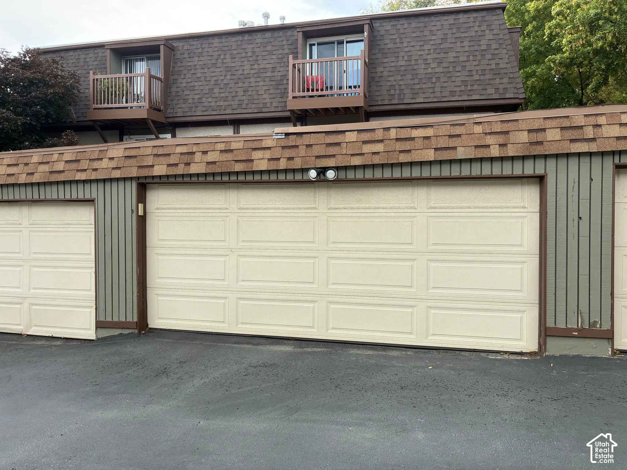 Multiple garage doors with paneling, upper-level balconies with wood railings, and a shingled roofline