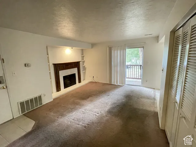 Living area featuring a fireplace with a wood-finish mantel and tile surround, built-in shelving, sliding glass door with vertical blinds, and louvered bifold doors