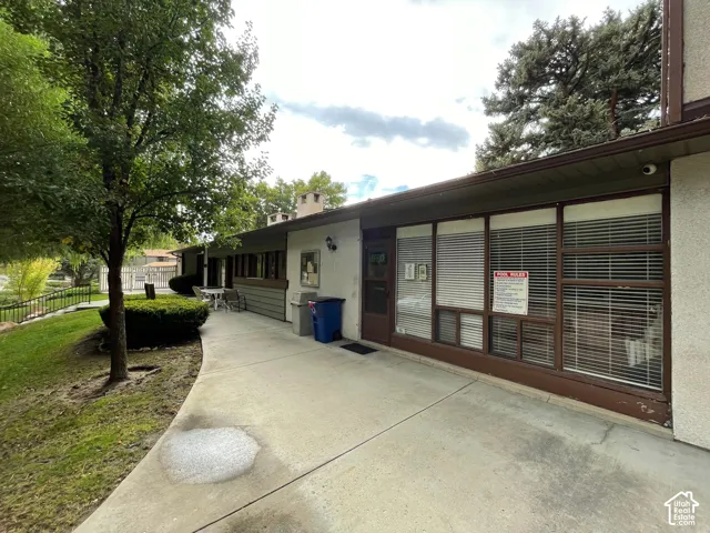 Exterior building with a concrete walkway, multiple windows with blinds, and a brown entry door