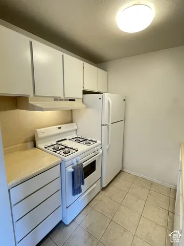 Kitchen featuring white cabinetry, beige countertops, gas range, refrigerator, and tile flooring