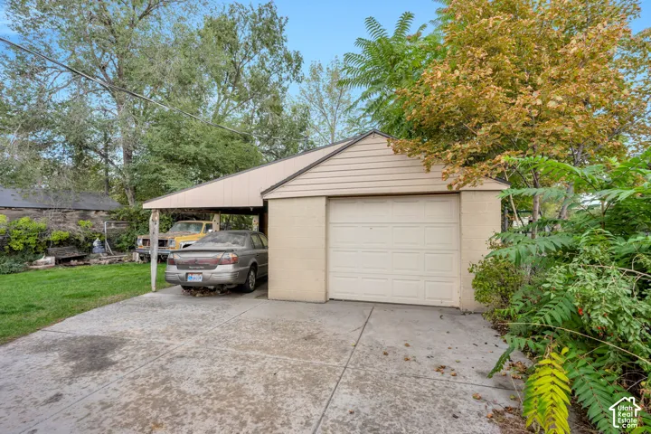 Detached garage with panel siding, an overhead door, and an attached carport
