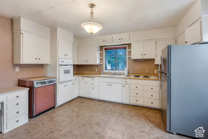 Kitchen featuring white cabinetry, built-in oven, integrated stovetop, and a stainless steel refrigerator