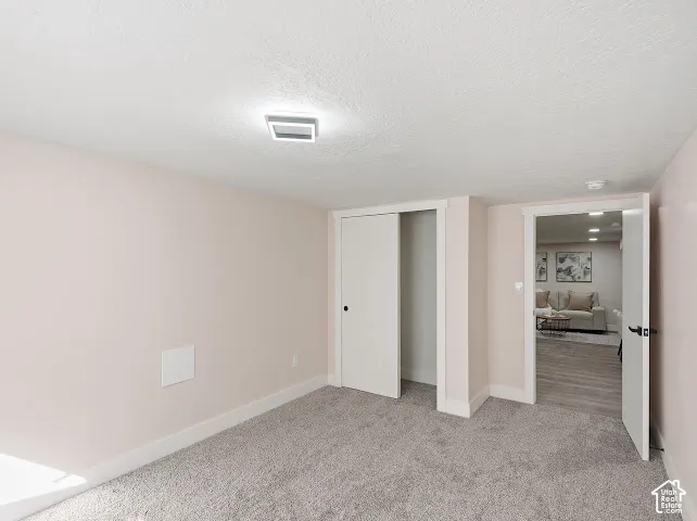 Neutral-toned interior space featuring light-colored wall paint, wall-to-wall carpeting, a square flush-mount light fixture, and a built-in closet with a sliding door