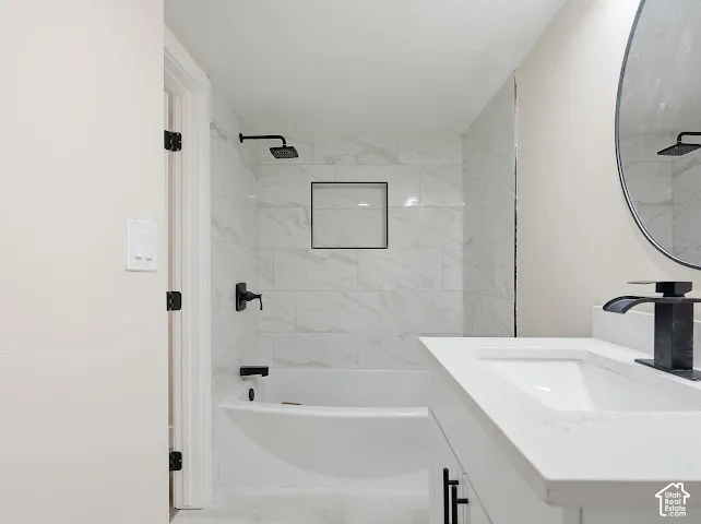 Bathroom featuring a white vanity with a quartz countertop, matte black faucet, oval wall-mounted mirror, and a tub-shower combination with floor-to-ceiling tile surround and built-in niche