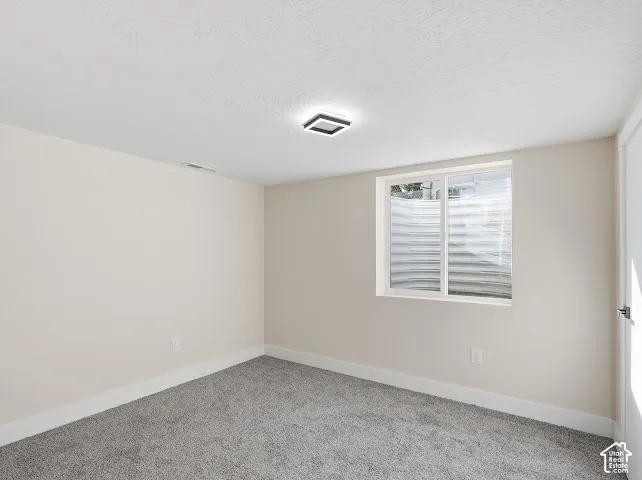 Neutral-toned walls, grey carpeting, flush-mount LED lighting, and a sliding window with a corrugated steel window well