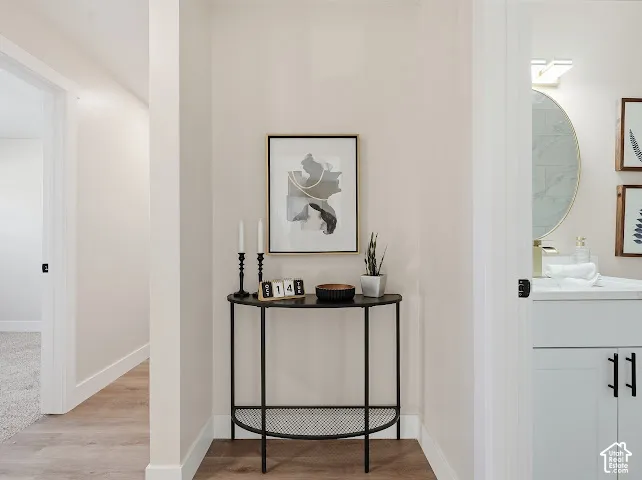 Neutral interior hallway with wood-finish flooring, white vanity featuring a rectangular vessel sink, round wall-mounted mirror, and matte black cabinet hardware