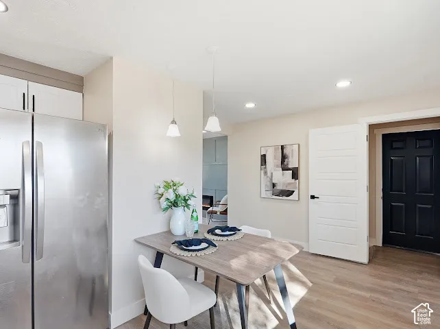 Kitchen area featuring stainless steel refrigerator, white cabinetry, dual pendant lighting, and wood-finish flooring