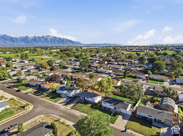 Aerial perspective of a suburban neighborhood featuring paved streets, established residential lots, mature trees, and a mountain backdrop