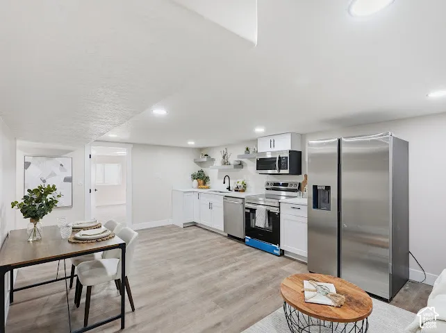 Kitchen featuring white cabinetry, stainless steel appliances, floating shelves, recessed lighting, and wood-finish flooring
