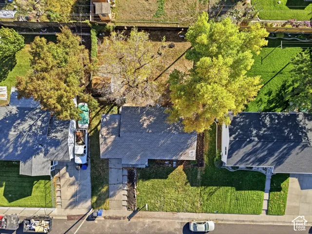 Aerial view of residential property featuring a pitched roofline, mature trees, grass lawn, and a concrete driveway