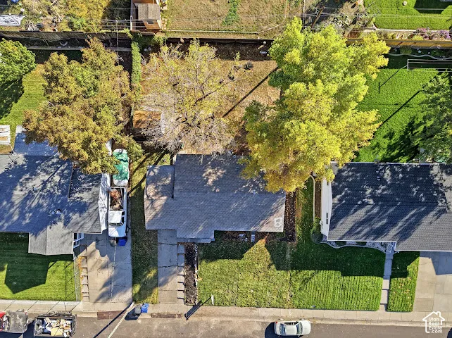 Aerial perspective featuring an asphalt shingle roof, concrete driveway, and mature trees situated on a rectangular lot with perimeter wood fencing