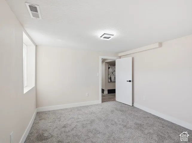 Neutral-toned interior room featuring wall-to-wall carpeting, a recessed window, a single-panel interior door with matte black hardware, and a square-profile ceiling light fixture