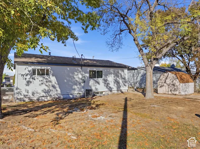 Rear exterior featuring horizontal vinyl siding, multi-pane windows, a storage shed, and mature trees