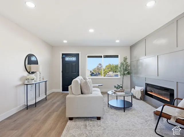 Living area featuring wood-finish flooring, recessed lighting, a fireplace with a decorative board-and-batten accent wall, and a black exterior door with a window insert