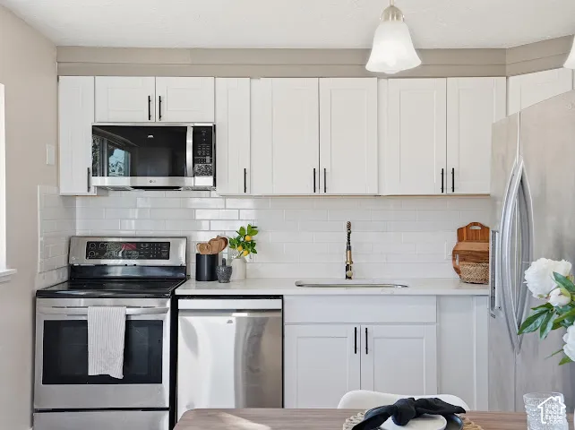 White shaker-style cabinetry with matte black hardware, stainless steel appliances, subway tile backsplash, and light-toned solid surface countertops
