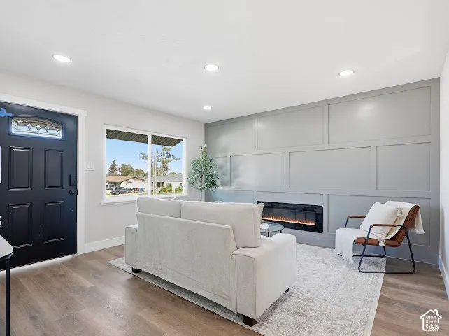 Living area featuring wood-finish flooring, a matte black entry door, recessed lighting, and a wall-mounted electric fireplace with custom paneling