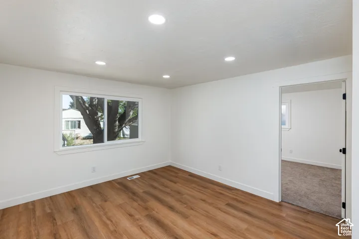Recessed ceiling lighting, wood-finish flooring, white trim, and a window with white casing