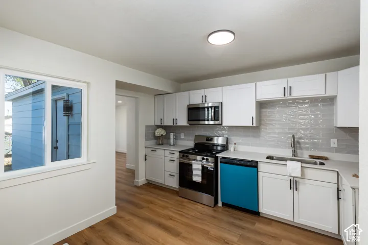 Modern kitchen featuring white shaker cabinets, stainless steel appliances, a white countertop, and wood-finish flooring