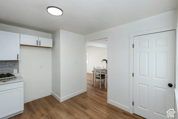 Wood-finish flooring, white cabinetry with black hardware, white countertops, and a gray subway tile backsplash
