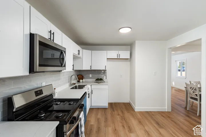 Kitchen featuring white cabinetry, light countertops, subway tile backsplash, stainless steel appliances, and wood-finish flooring