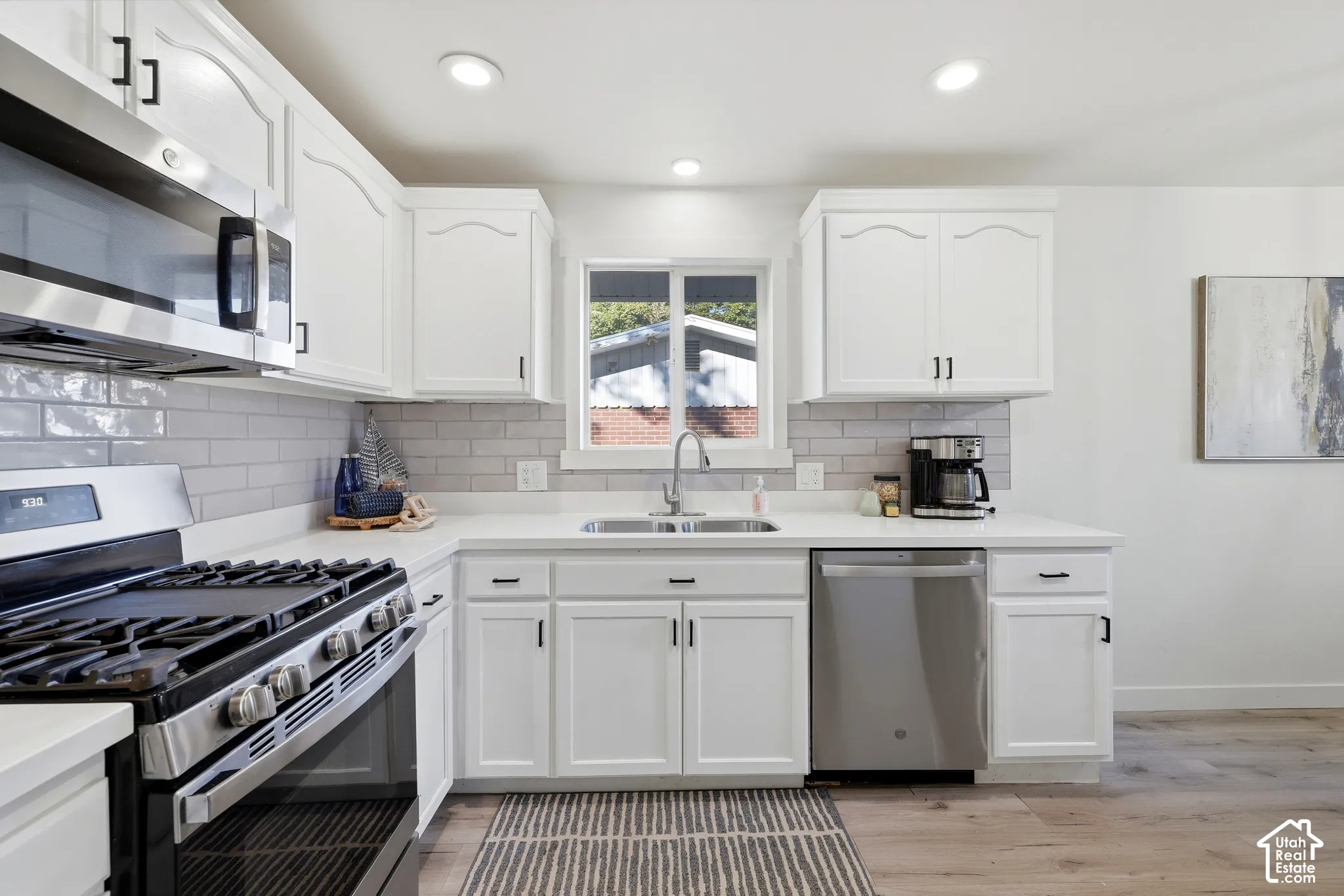 White shaker-style cabinetry with black hardware, stainless steel appliances, light-toned countertops, subway tile backsplash, and recessed lighting