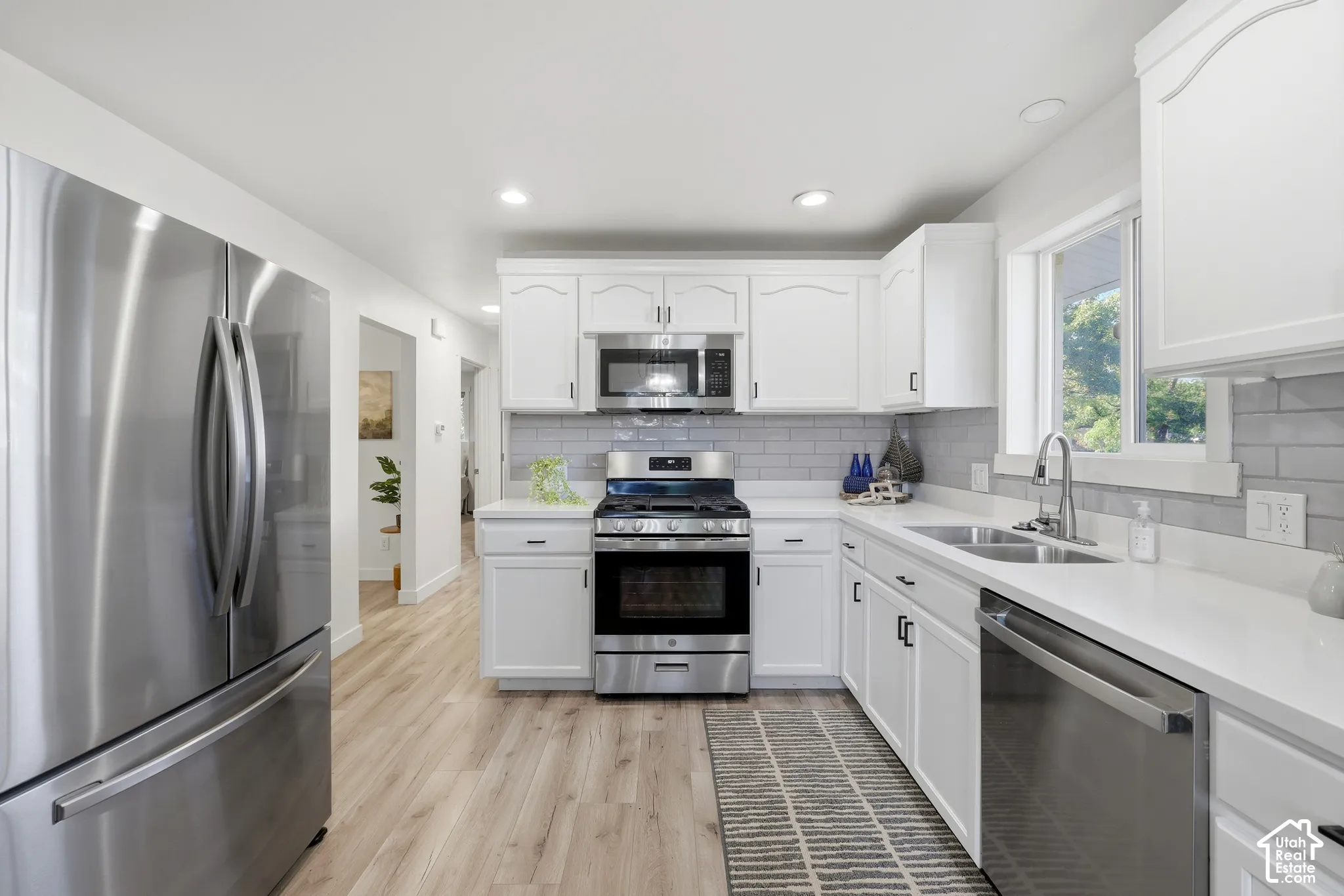 Kitchen featuring white cabinetry, light-toned wood-finish flooring, stainless steel appliances, a double basin sink, and a tiled backsplash