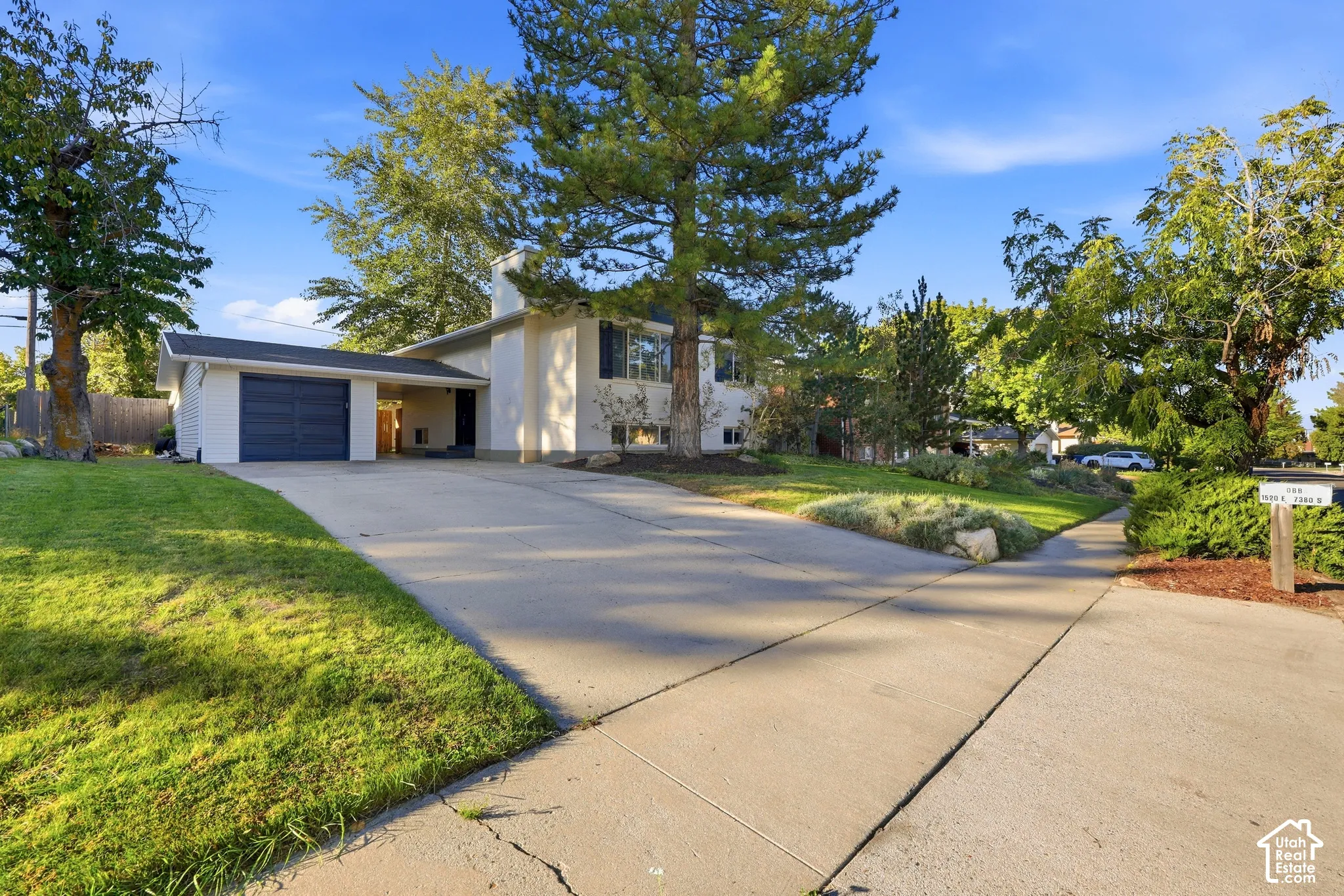 Two-story residence featuring a two-car garage with an overhead door, an extended concrete driveway, and mature landscaping