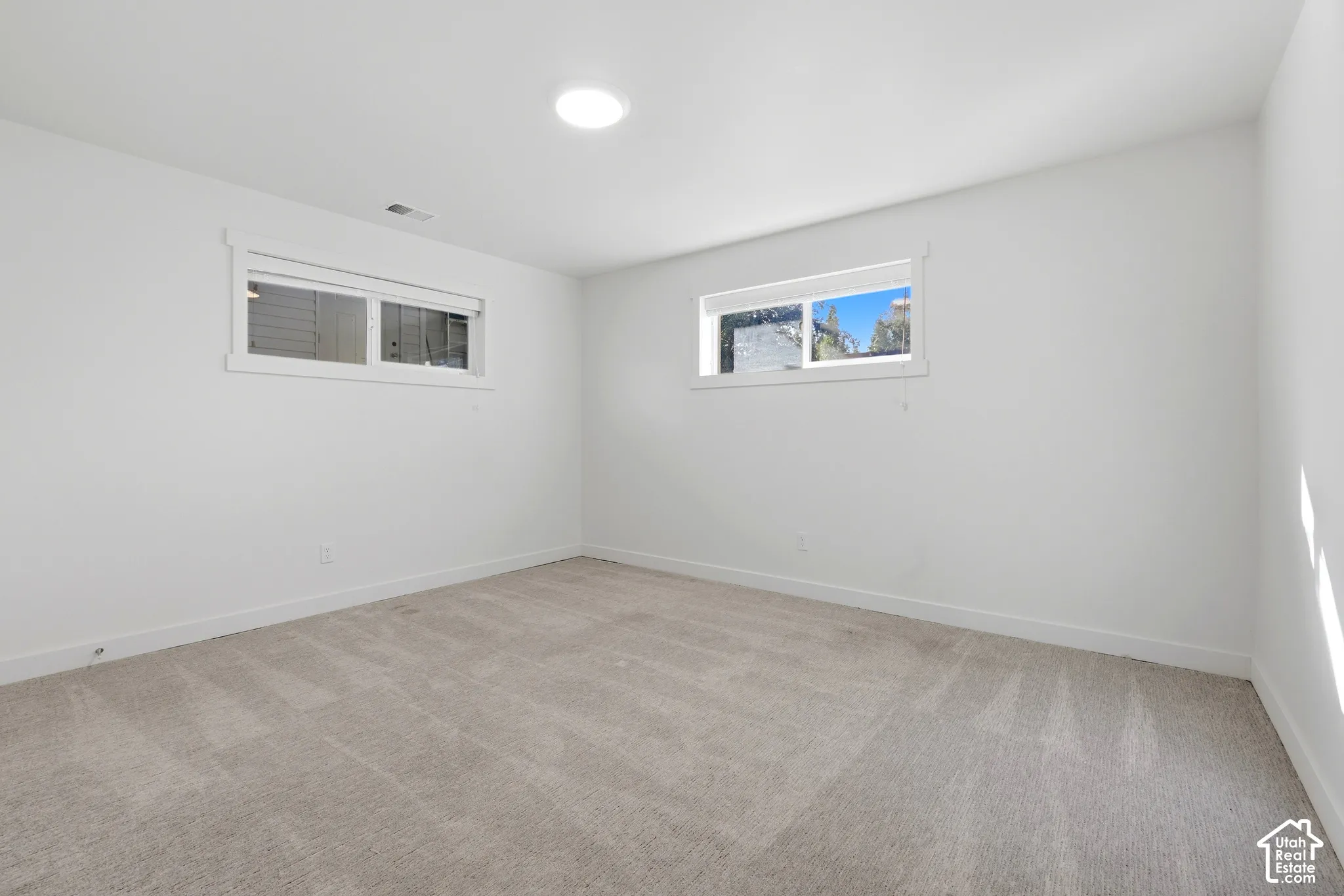 Recessed ceiling light, two windows with white trim, light-colored carpeting, and white walls