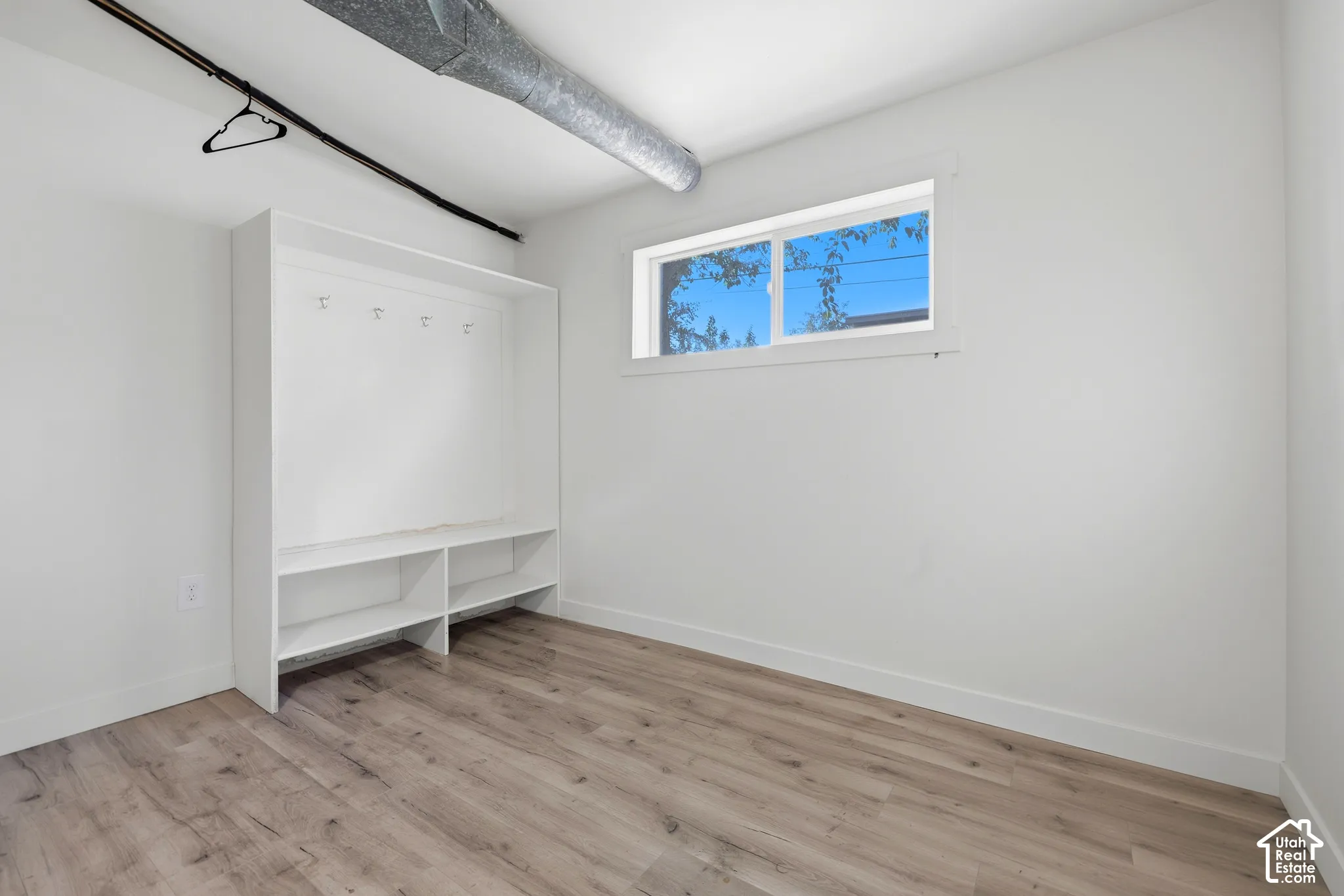 Built-in storage unit with hooks and shelving, wood-finish flooring, white walls, and a window with white trim