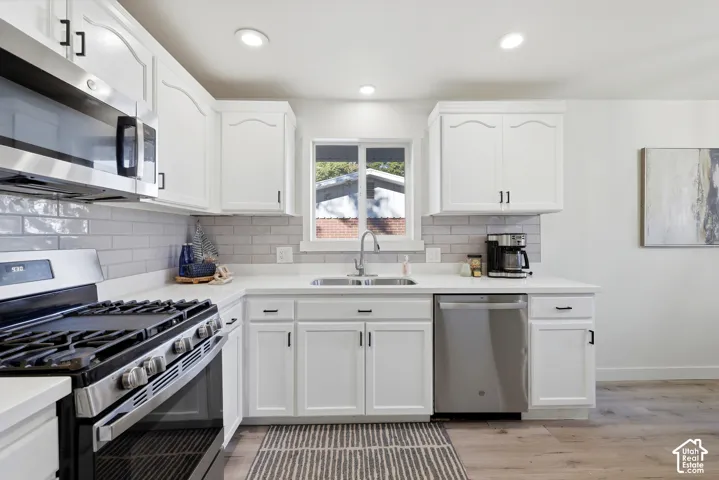 White shaker-style cabinetry with black hardware, stainless steel appliances, light-toned countertops, subway tile backsplash, and recessed lighting