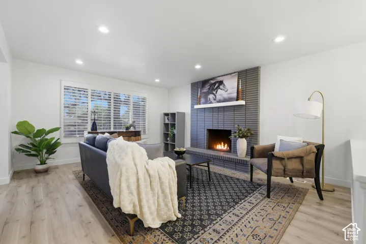 Recessed lighting, wood-finish flooring, white plantation shutters, and a fireplace with a gray brick surround and white mantel