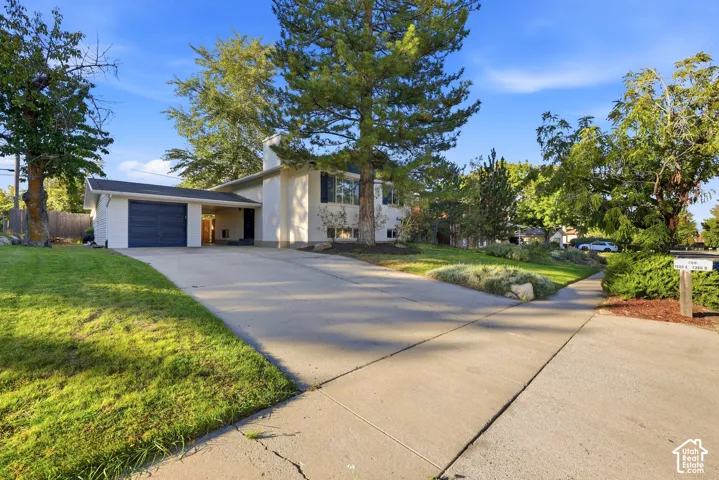 Two-story residence featuring a two-car garage with an overhead door, an extended concrete driveway, and mature landscaping