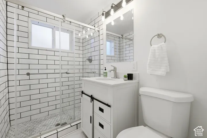 White subway tile shower with a sliding glass door, white hex tile shower floor, single vanity with a white countertop and brushed nickel faucet, and a toilet