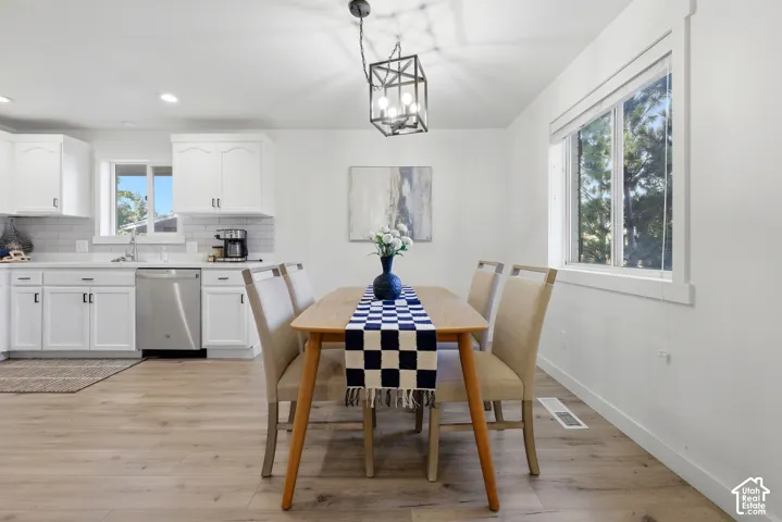 Open concept living area featuring wood-finish flooring, white cabinetry, a subway tile backsplash, and a modern pendant light fixture
