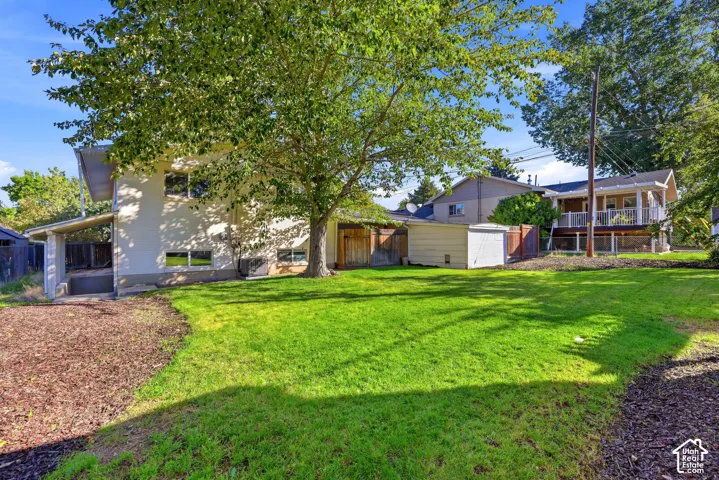 Expansive lawn area with mature trees, featuring a detached storage shed and a covered carport