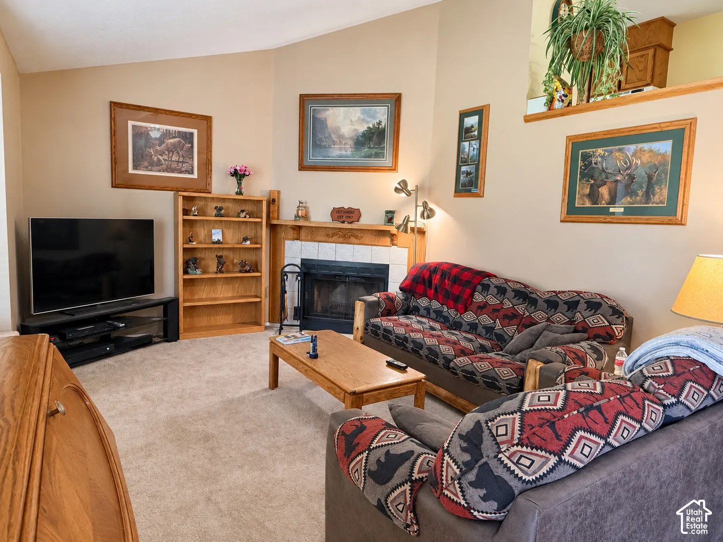 Comfortable family room featuring warm wood-finish cabinetry, a wood-burning fireplace with surround, neutral carpeting, and ample natural lighting from multiple windows