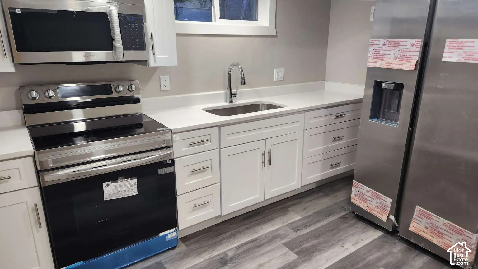 White cabinetry, stainless steel appliances, solid surface countertops, single basin sink, and wood-finish flooring