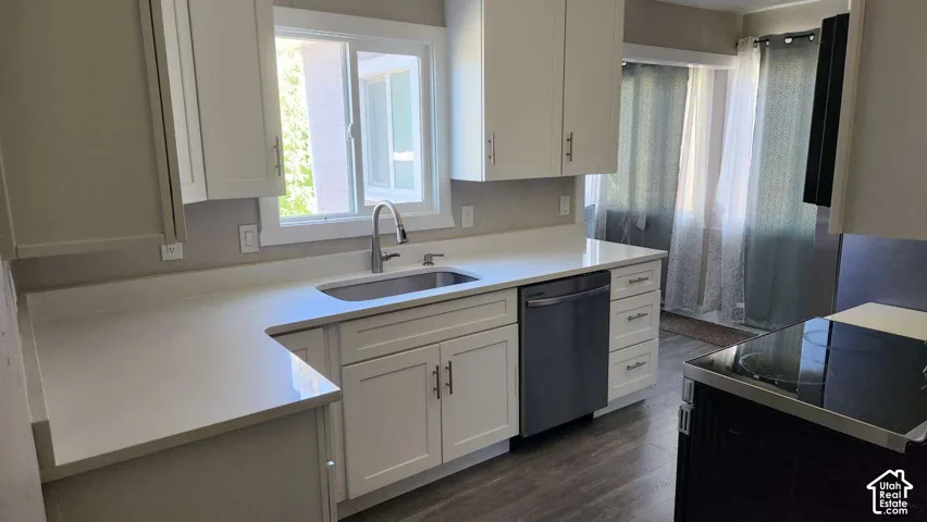 White shaker-style cabinetry with T-bar hardware, light-toned countertops, a stainless steel undermount sink, and a stainless steel dishwasher