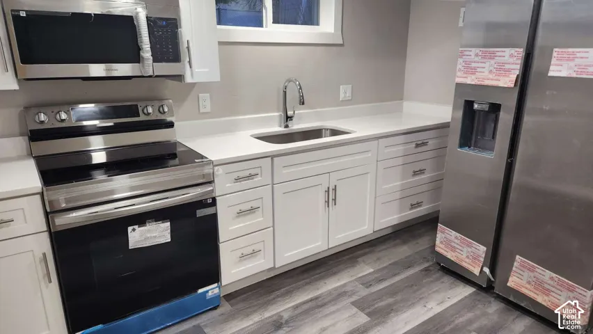 White cabinetry, stainless steel appliances, solid surface countertops, single basin sink, and wood-finish flooring