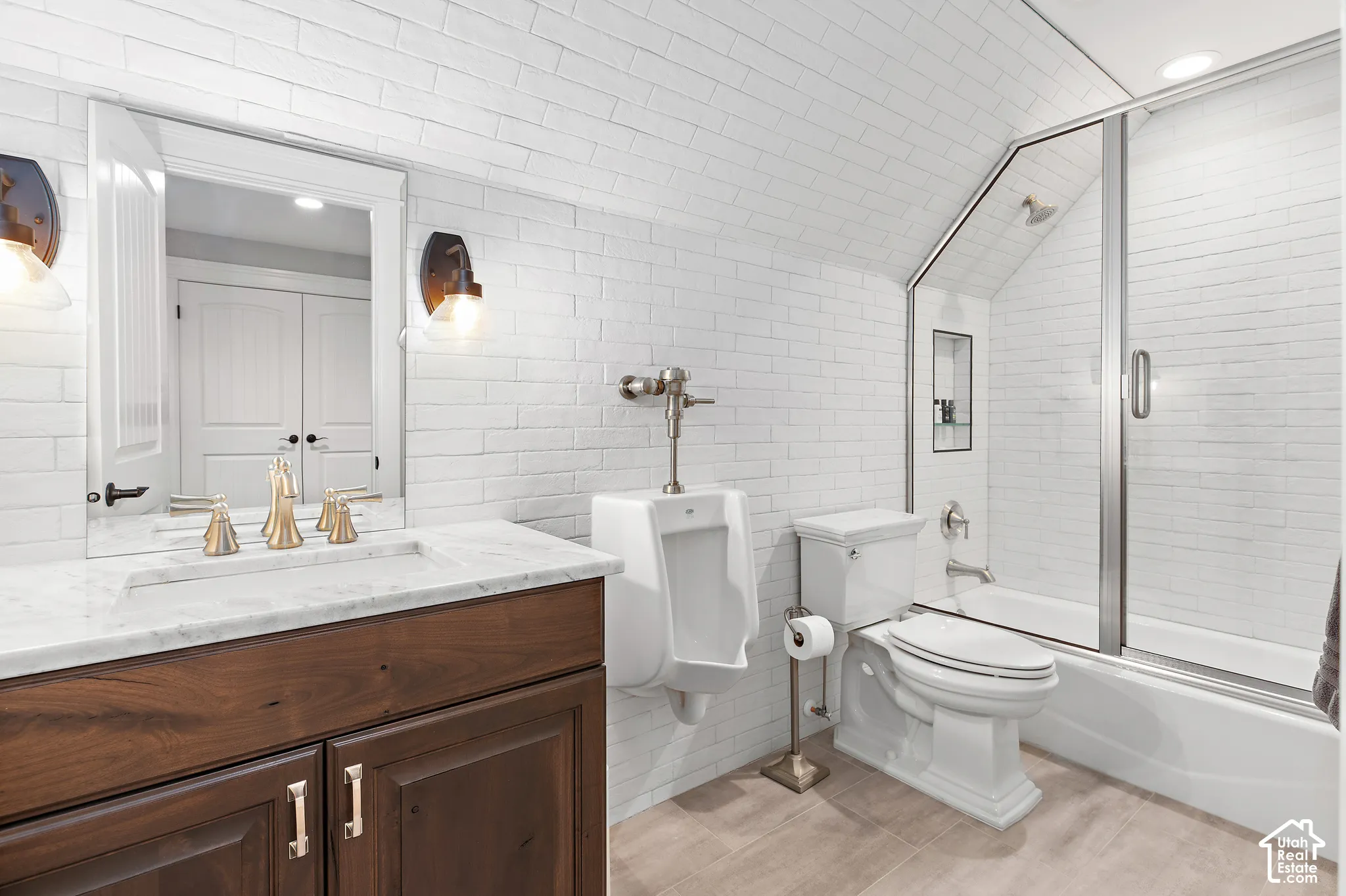 White subway tile walls with an angled ceiling, dark wood-finish vanity with a white countertop, built-in mirror, and a full bathtub with a glass enclosure